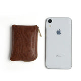 Brown crocodile-patterned coin pouch next to a silver iPhone on a white background