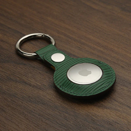 Green textured leather AirTag keychain with metal ring on wood surface