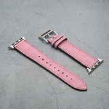 Pink crocodile skin watch band with silver buckle on a gray surface