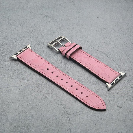 Pink crocodile skin watch band with silver buckle on a gray surface