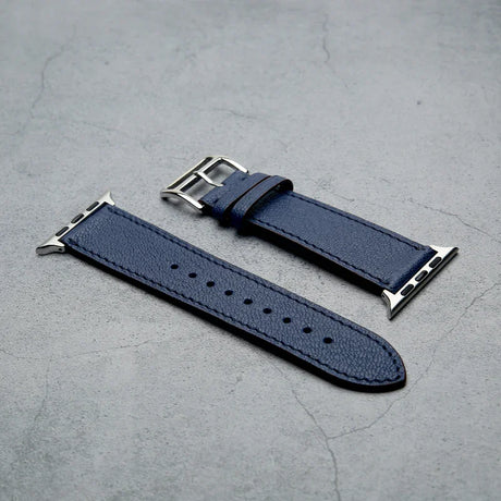 Blue leather watch strap with silver buckle on a gray surface
