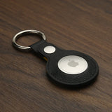 Black leather saffiano keychain with a metallic Apple logo on a wooden surface