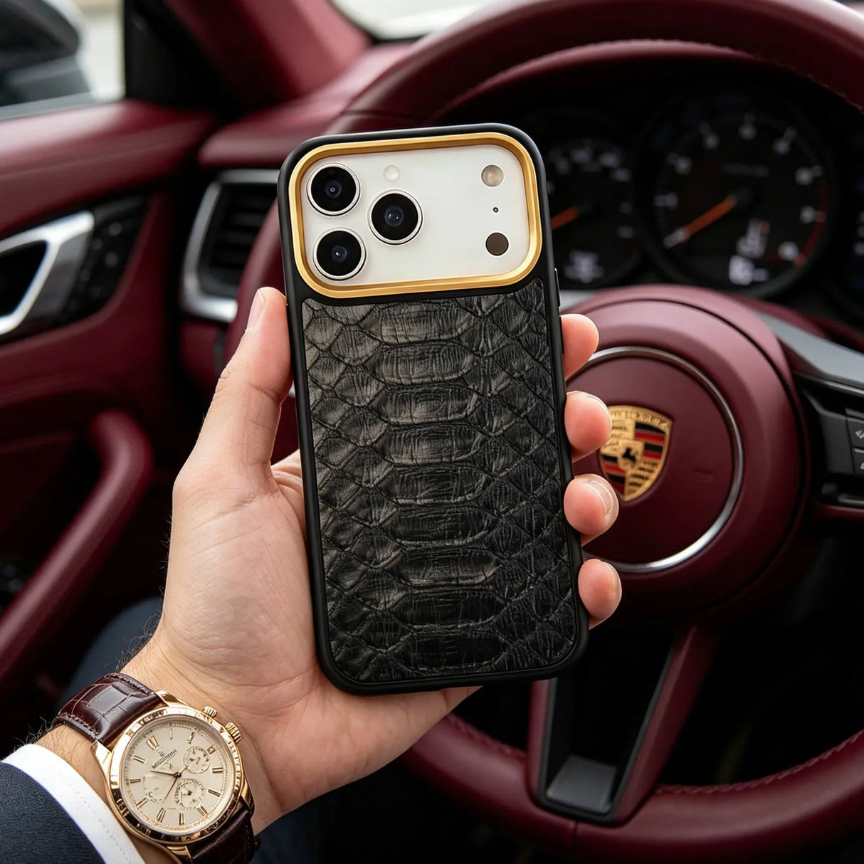 Hand holding an iphone 17 pro case with a python skin  in front of a car's steering wheel.