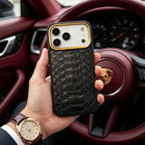 Hand holding an iphone 17 pro case with a python skin  in front of a car's steering wheel.