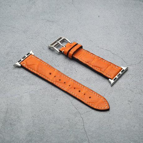 Orange watch strap with silver buckle on a gray surface