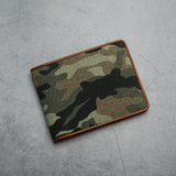 Camouflage canvas wallet with brown trim on a gray concrete surface