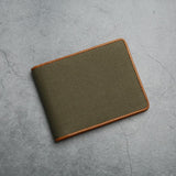 Green canvas wallet with brown trim on a gray concrete surface