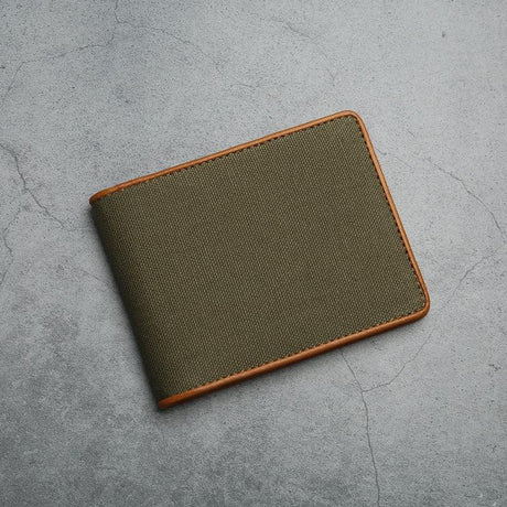 Green canvas wallet with brown trim on a gray concrete surface