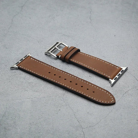 Brown vegetable tanned leather watch strap with silver buckle on a gray surface
