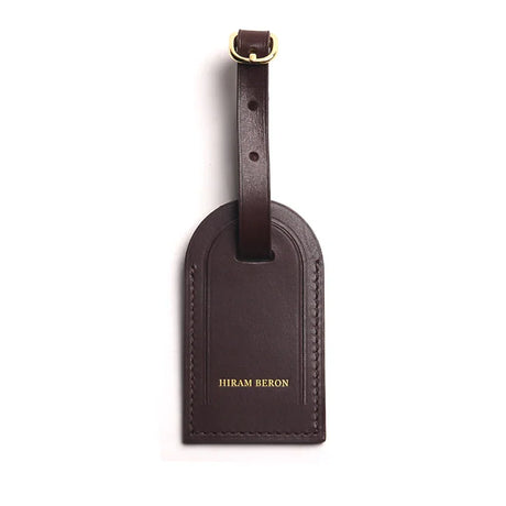coffee brown leather luggage tag with a gold buckle on a white background
