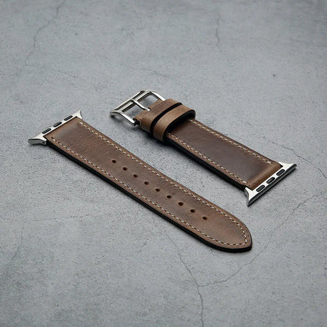 Brown leather watch strap with silver metal clasp on a gray surface
