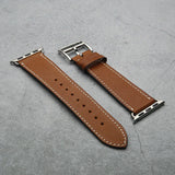 Brown leather watch strap with silver buckle on a gray surface