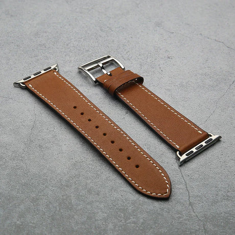 Brown leather watch strap with silver buckle on a gray surface