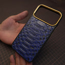 Blue python skin phone case with gold accents held by a hand on a dark surface.