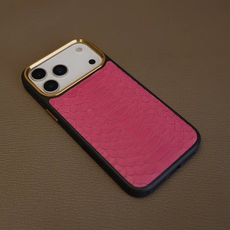 Pink snakeskin iPhone case with gold camera trim on leather surface