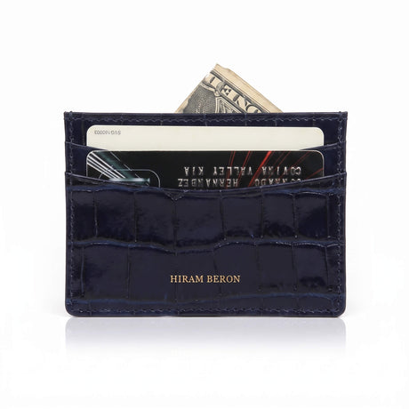 A navy blue patent crocodile leather card holder wallet with gold-foiled 'HIRAM BERON' branding on the front, shown with credit cards and cash partially inserted against a white background.