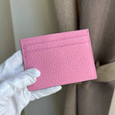 Pink pebble leatger cardholder held by a gloved hand against a neutral background
