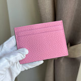Pink pebble leatger cardholder held by a gloved hand against a neutral background