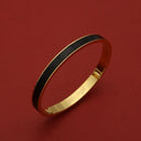 Gold bangle with black enamel inlay, engraved 'OROLOGII', luxury minimalist design on red background