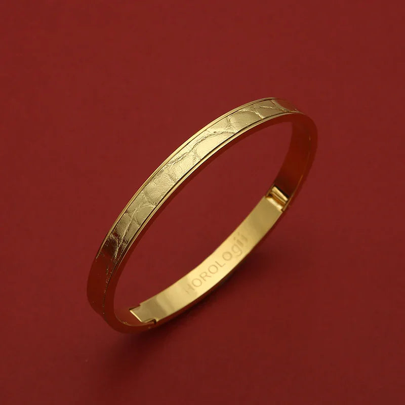 Gold bangle with textured pattern and engraved HOROLOGII, luxury accessory on red background