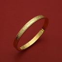 Gold bangle with textured pattern and engraved HOROLOGII, luxury accessory on red background