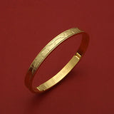Gold bangle with textured pattern and engraved HOROLOGII, luxury accessory on red background