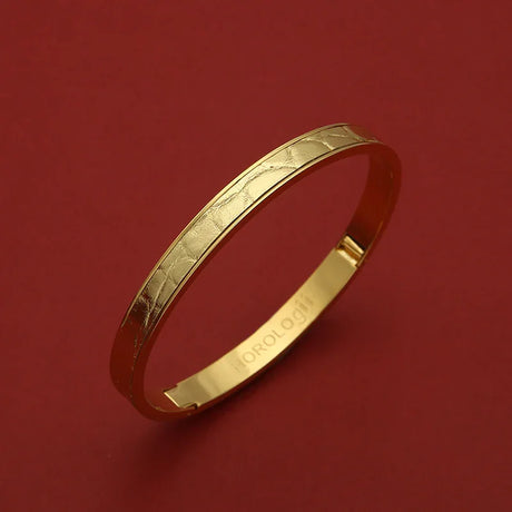 Gold bangle with textured pattern and engraved HOROLOGII, luxury accessory on red background