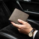 Hand holding a pebble grey wallet with a watch on a car seat background