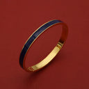 Gold bangle with navy blue enamel inlay, luxury bracelet for women, elegant accessory on red background