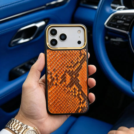 Hand holding an iphone 17 pro case with orange snake skin pattern in a luxury car interior