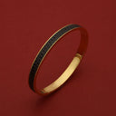 Gold bangle with black textured inlay, engraved 'HOROLOGII', luxury accessory on red background